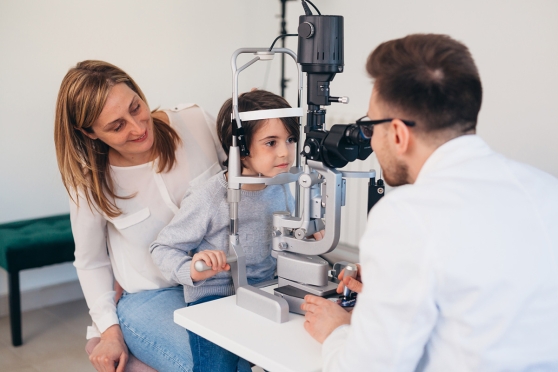A child getting an eye exam from an eye doctor with his mother watching 
